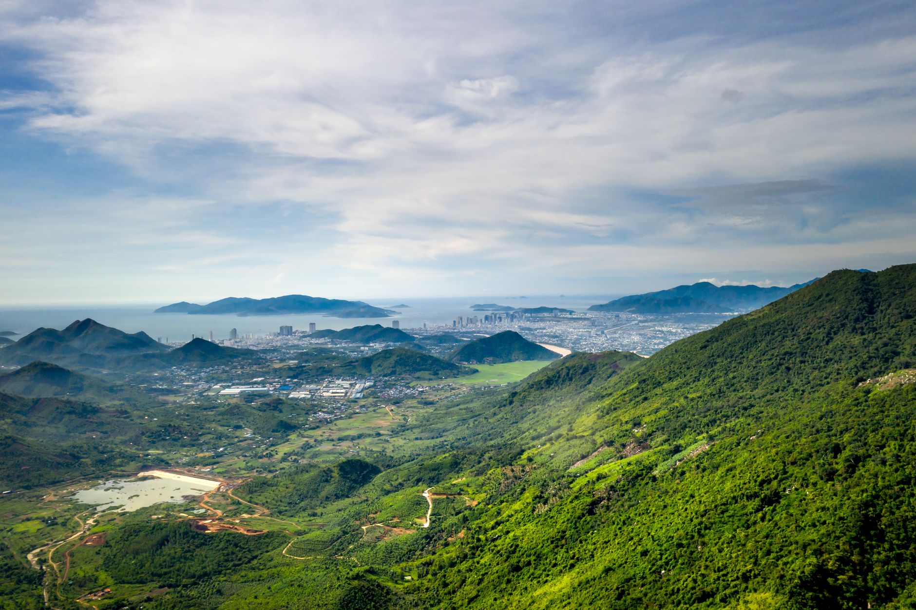 Breathtaking landscape view of a city nestled between lush mountains and the coastline, captured in daylight.