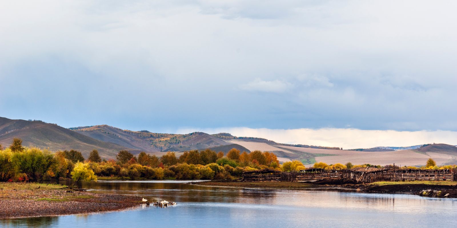 A tranquil river flowing through rolling hills with vibrant autumn foliage