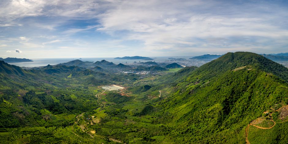 A breathtaking aerial panorama of verdant mountains and coastline under a clear blue sky.