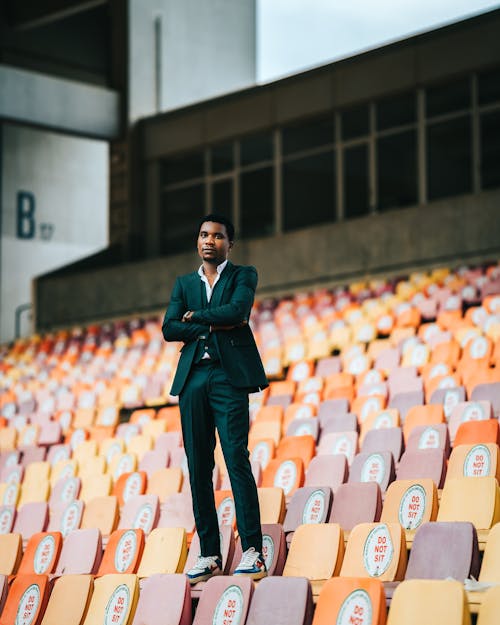 Man in Black Suit Jacket Standing on Empty Bleachers in Auditorium