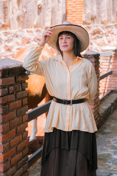 Free Elegant woman wearing a wide-brimmed hat and stylish outfit posing confidently in an outdoor rustic setting. Stock Photo
