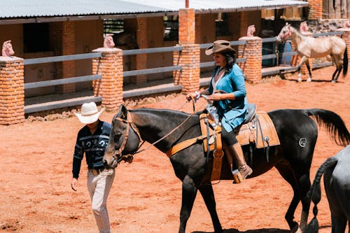 Woman Wearing a Cowboy Hat Riding a Horse with a Man Beside Her in a Ranch  