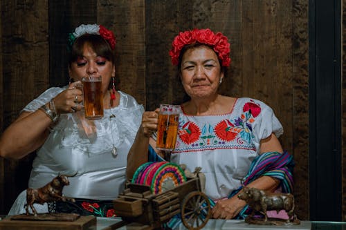 Woman in White Dress Wearing Red Green and White Headdress Drinking Beer