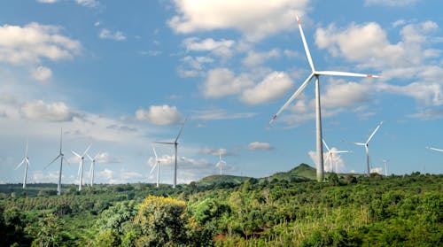 An Aerial Photography of Windmills Near the Green Trees Under the Blue Sky and White Clouds