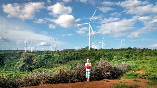 Free Woman exploring a rural area with wind turbines in a lush summer landscape. Stock Photo