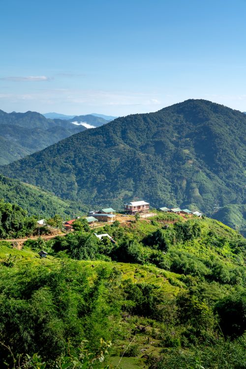 Free A picturesque rural village nestled in lush green hills with a majestic mountain backdrop. Stock Photo
