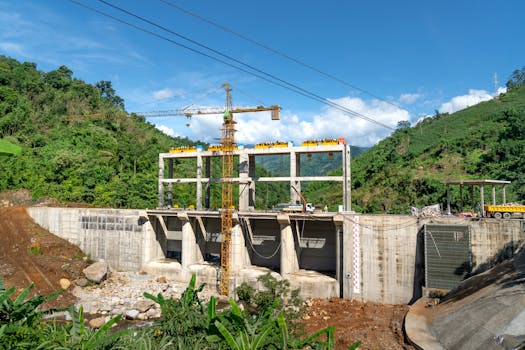 Crane operating at a construction site in a lush, mountainous area under bright blue skies.