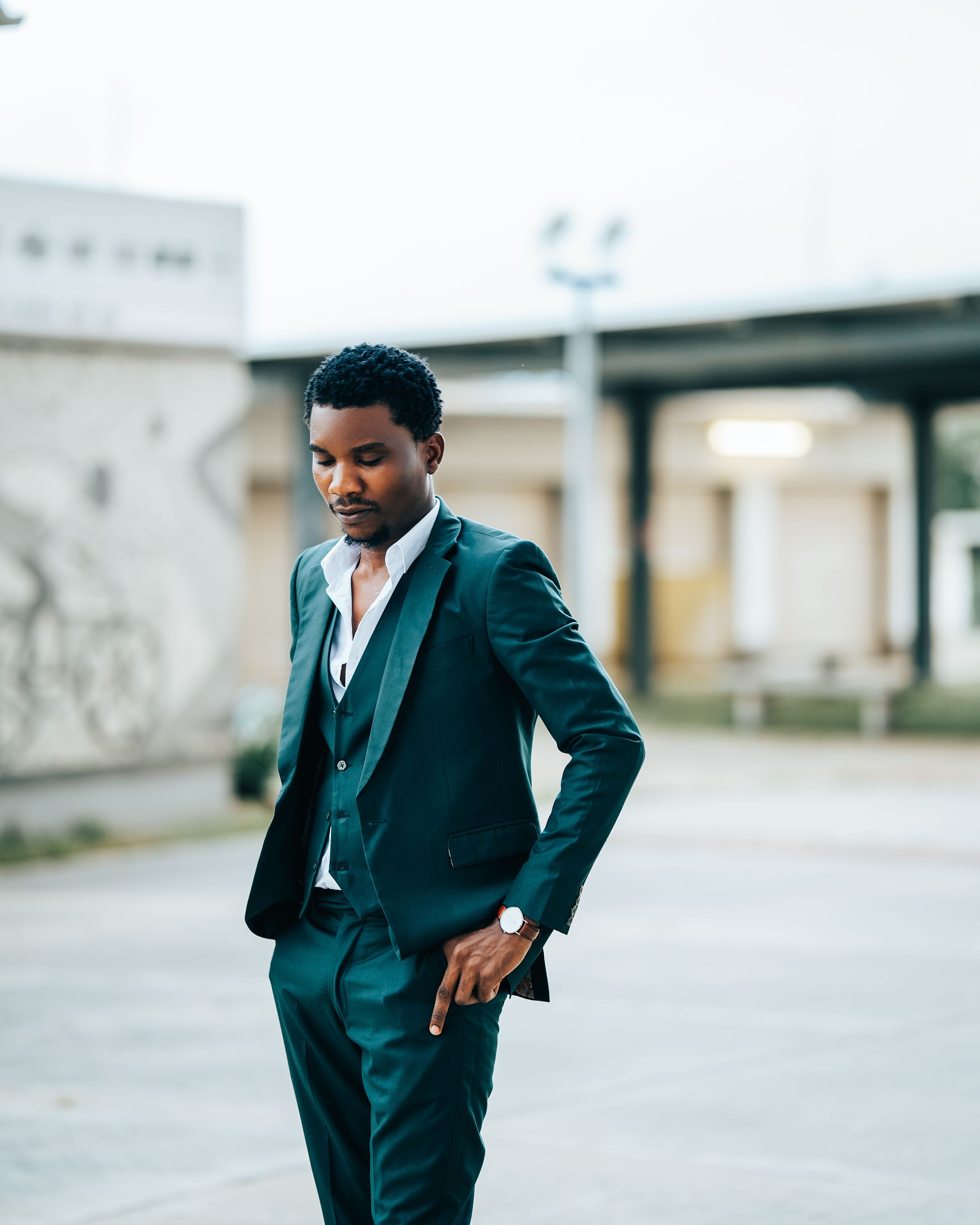 A man in a dark three-piece suit stands in a quiet courtyard in Abuja, the jacket unforced.