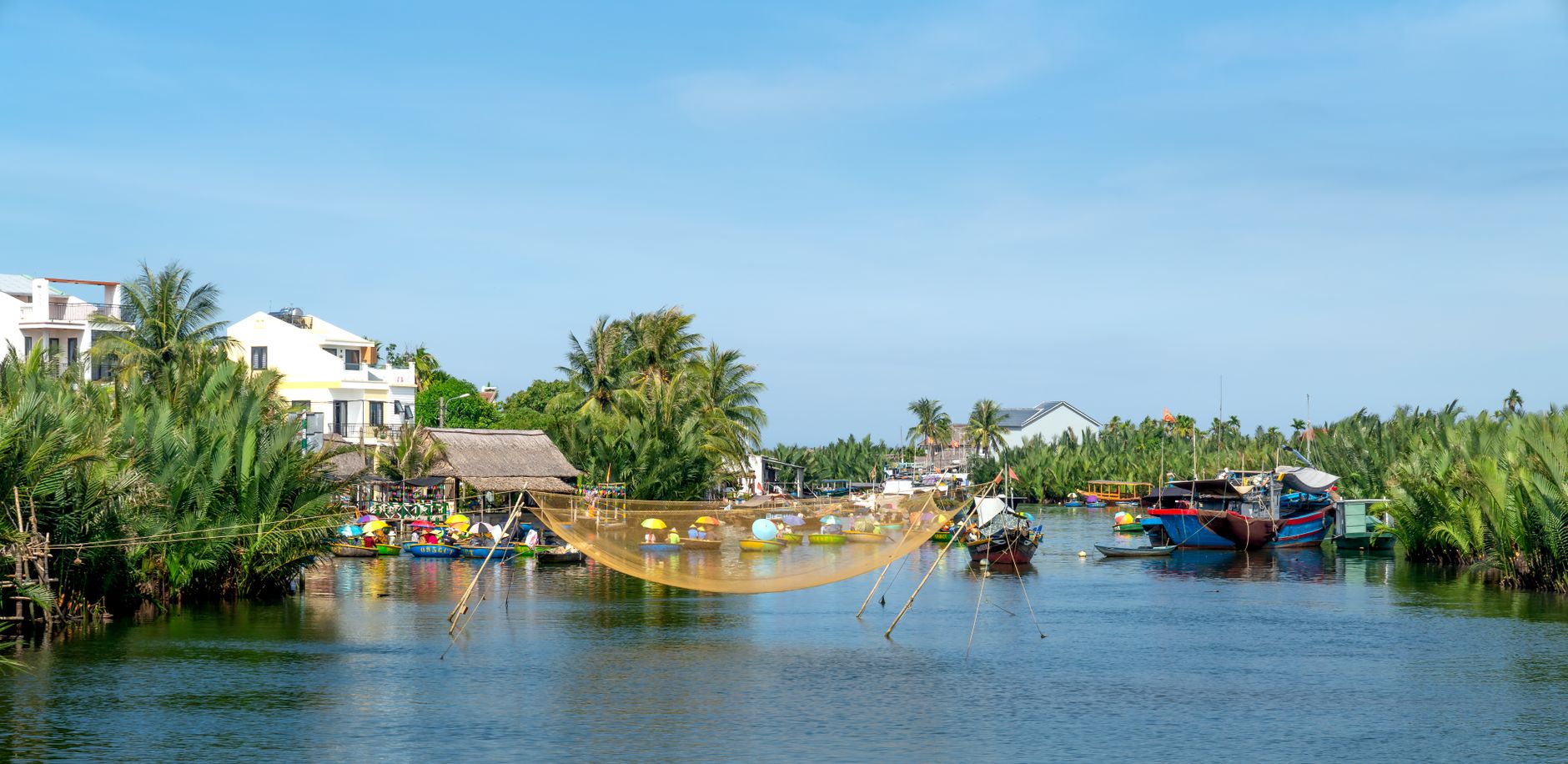 Scenic view of a tropical village by the river with boats and traditional fishing nets.