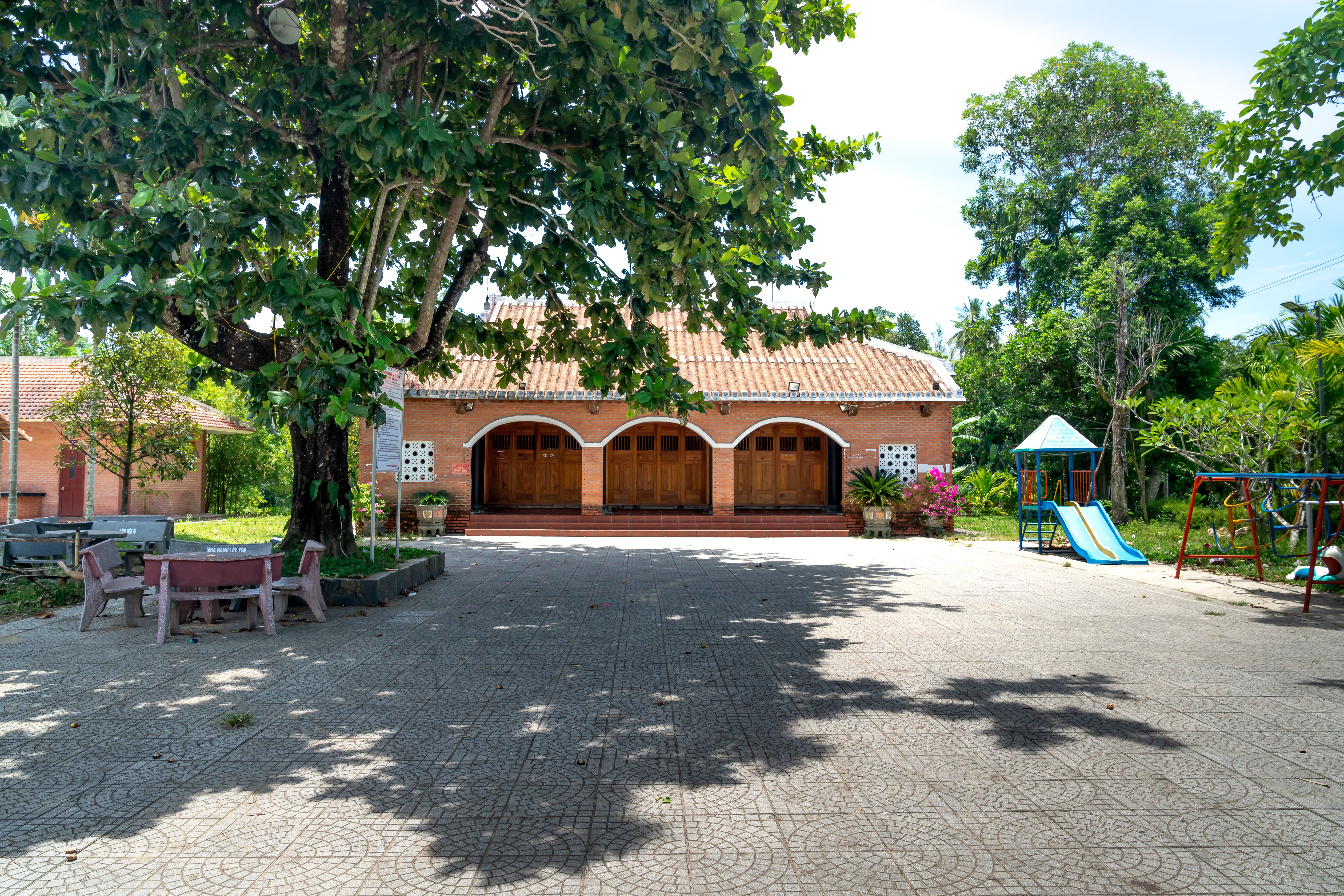 A serene backyard featuring a playground, tree, and brick house under a clear sky.