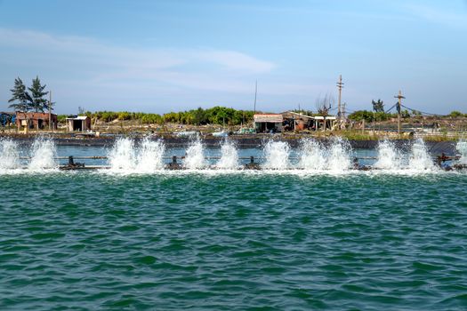 Aquaculture farm aerators creating ripples and splashes, under clear blue skies.