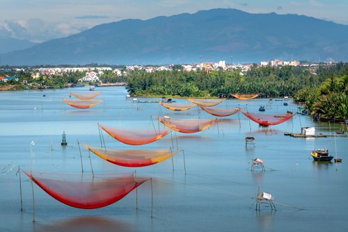 Free Vibrant fishing nets stretch across a serene lake near a lush town with distant mountains. Stock Photo