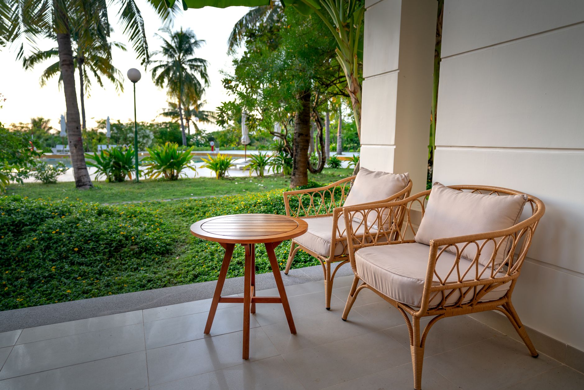 Peaceful veranda setting with rattan chairs and table, surrounded by lush palm trees and greenery.