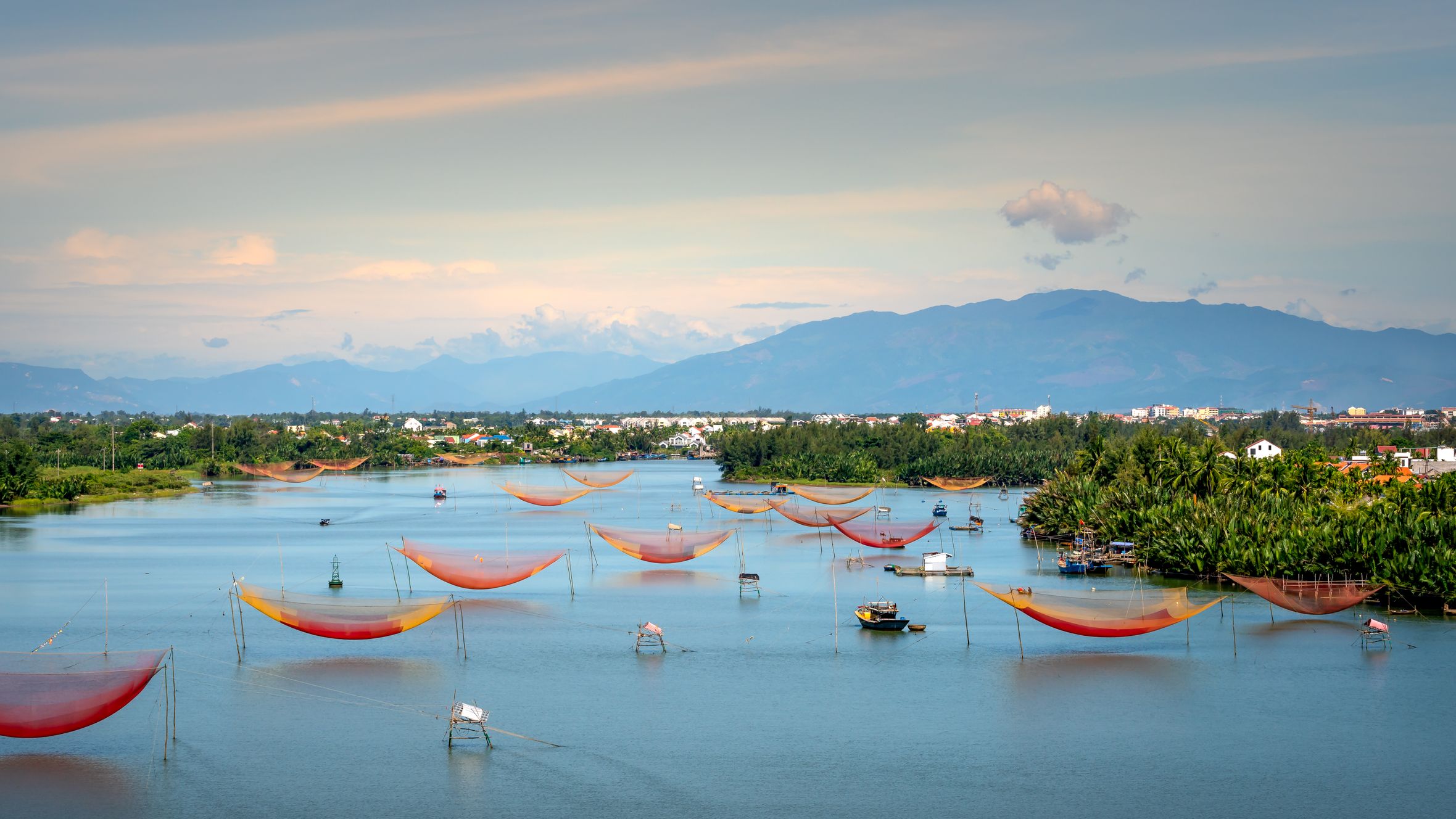 Stunning aerial view of colorful fishing nets on a tranquil river with lush greenery and distant mountains.