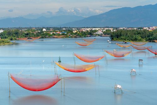 Free Scenic view of vibrant fishing nets over a serene river with a town and mountains in the backdrop. Stock Photo