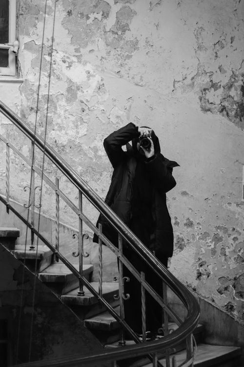 Free A photographer in black attire taking a picture in a rustic stairwell. Stock Photo