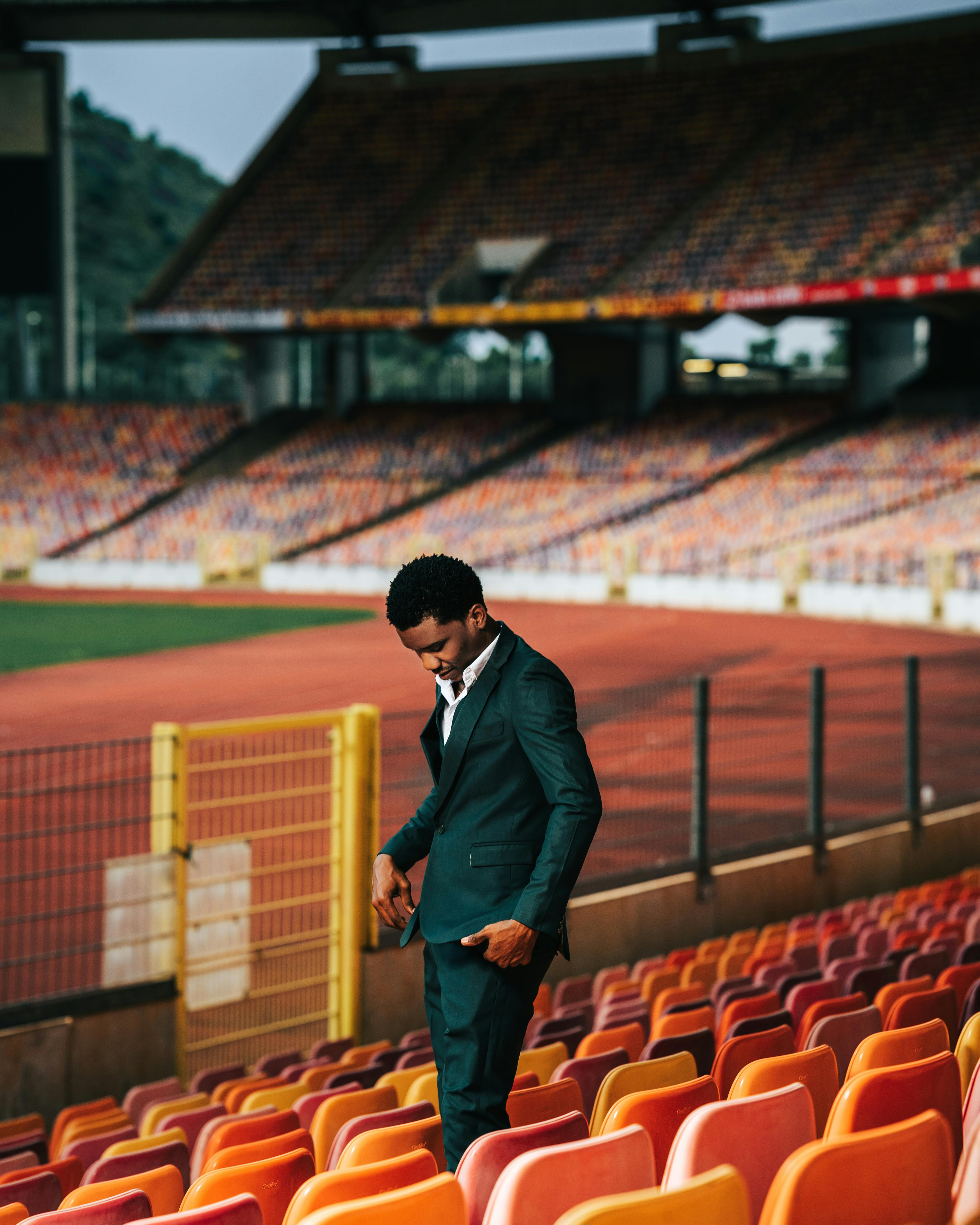 A man in a suit stands in an empty stadium, creating a striking fashion statement.