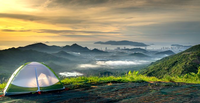 Peaceful campsite with tent overlooking scenic mountains and city at sunset.