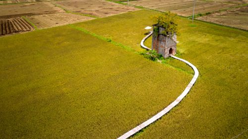 Free Aerial view of a rustic tower surrounded by green fields, with a winding path. Stock Photo