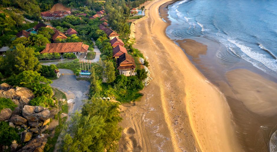 Aerial photograph of a picturesque beachfront village lined with greenery.