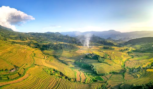 Free A breathtaking aerial view of golden rice terraces set against a mountainous backdrop. Stock Photo