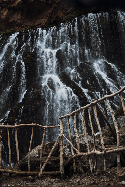 Free Majestic waterfall cascading behind a rustic wooden fence, surrounded by rocks. Stock Photo