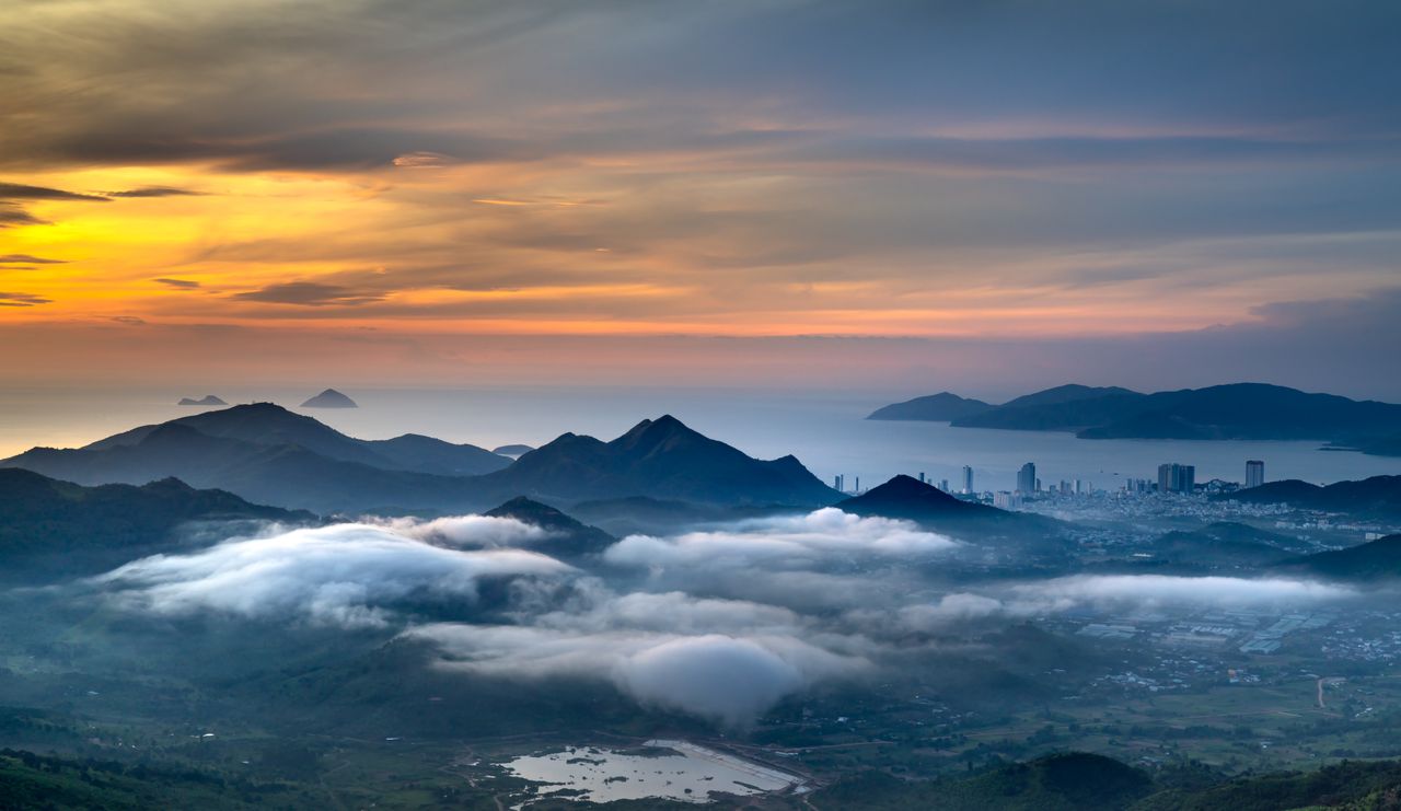 a breathtaking aerial view of mountains clouds and coastal city at sun