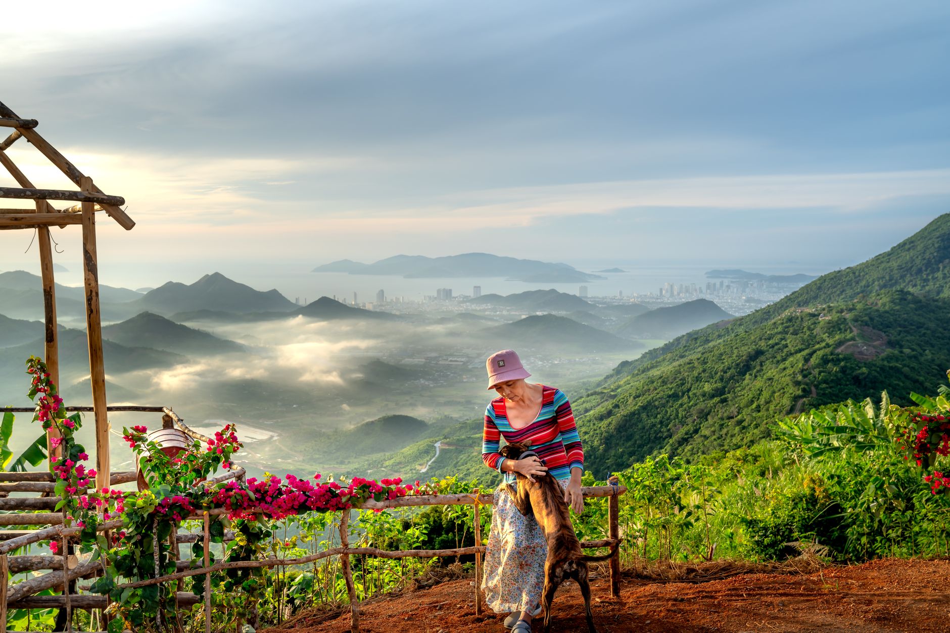 A woman in a striped shirt enjoys a scenic mountain view with her dog.