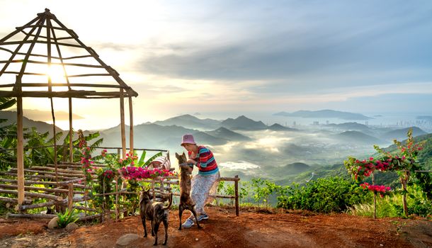 A woman enjoys a beautiful sunrise on a mountain with her dogs, surrounded by stunning landscapes.