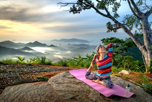 Free Senior woman practices yoga outdoors on a mountain at sunset, embracing wellness and serenity. Stock Photo