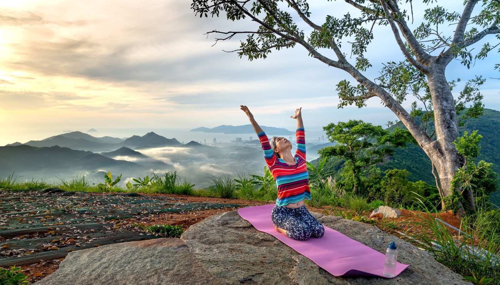 Woman practicing yoga outdoors at sunrise on a hilltop with a mountain view