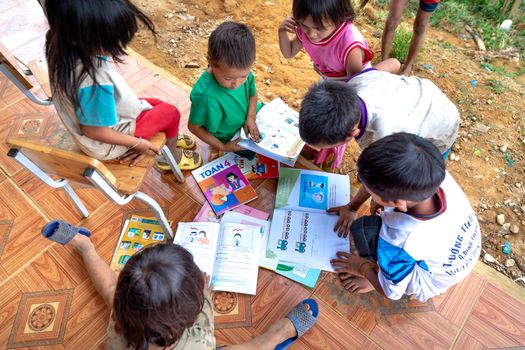 Children gathered on the ground exploring educational books together, promoting collaborative learning.