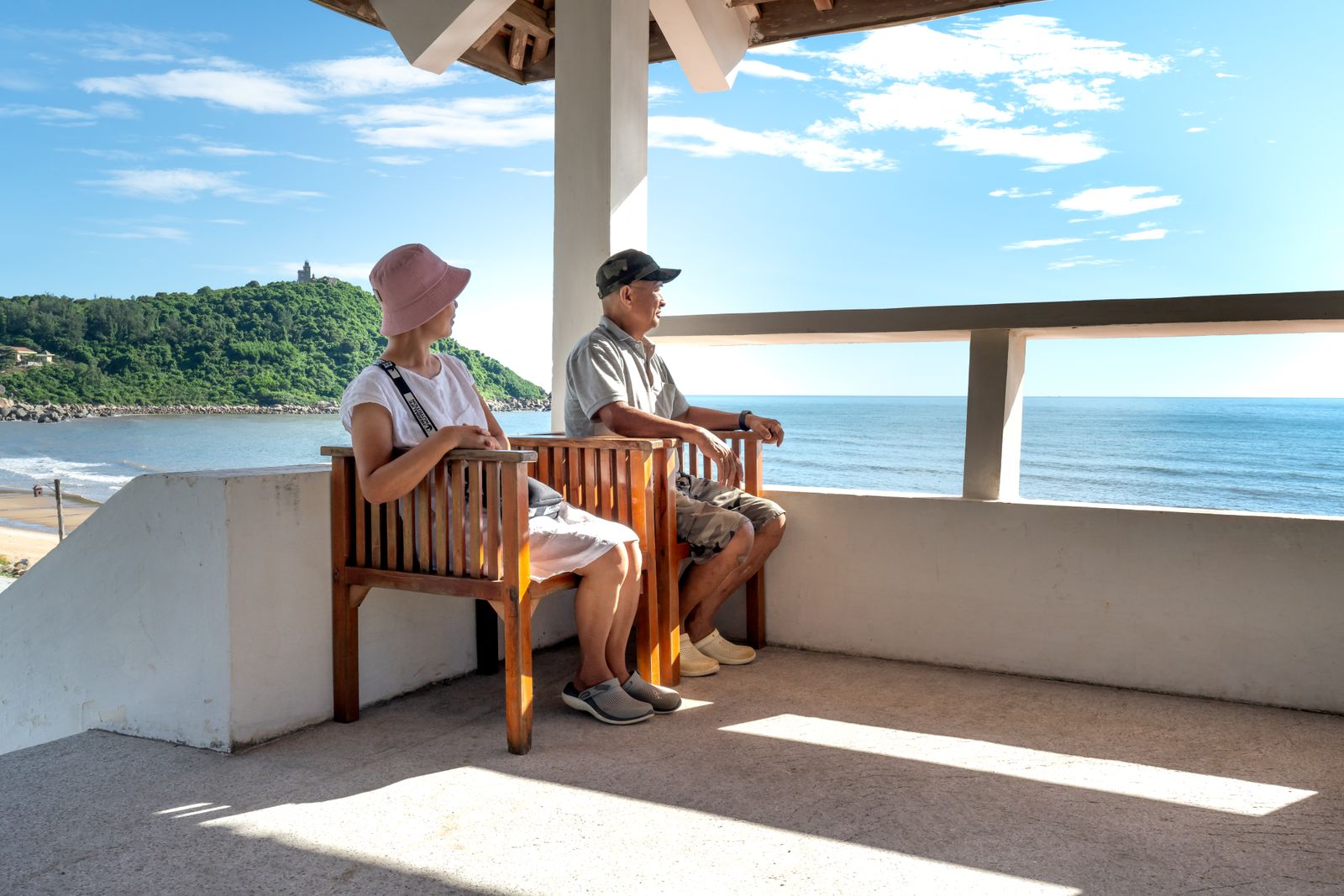 Senior couple sitting on balcony chairs, enjoying a relaxing ocean view in summer