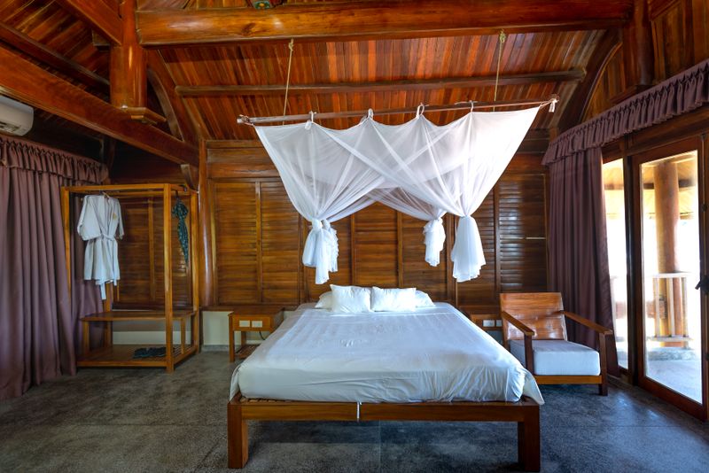 Interior de bungalow tipo suite con cama king bajo dosel, paredes de madera tropical y acceso a terraza
