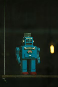 Close-up of a vintage blue toy robot standing alone on a dark shelf.