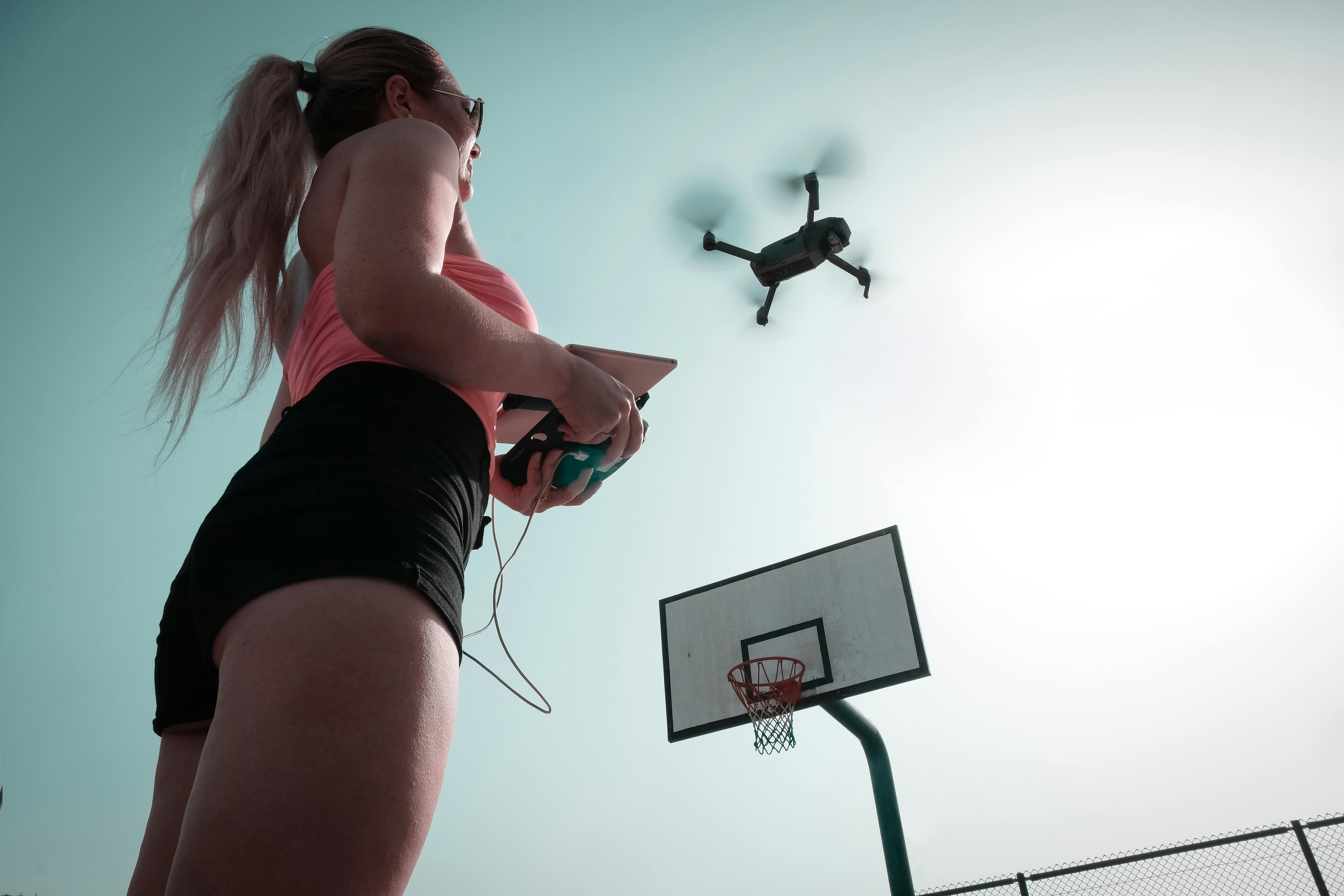 woman standing near basketball hoop controlling drone