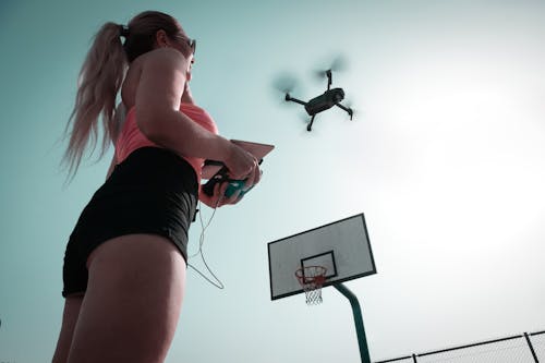 Kobieta, Stojąca W Pobliżu Obręczy Do Koszykówki, Kontrolująca Drona