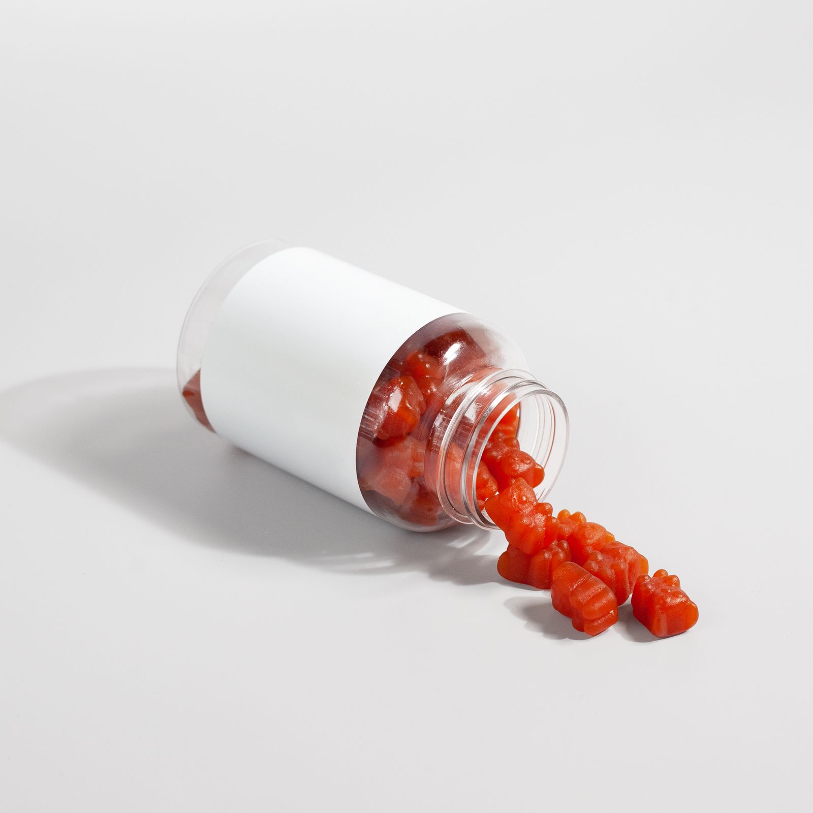 Fiber gummies spilling from an open supplement bottle onto a plain white surface
