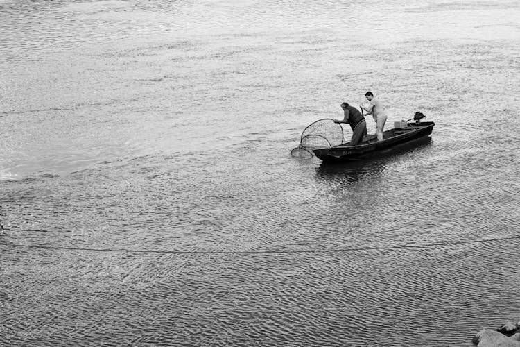Men Pulling A Fishing Net From Water While Standing On A Boat 