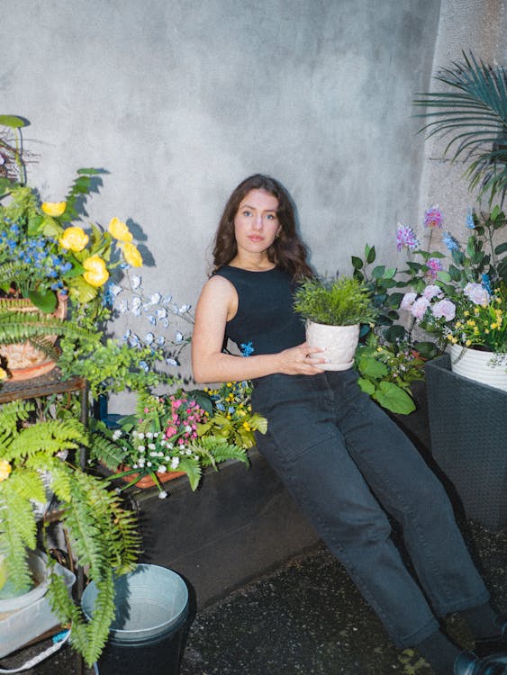 Woman in Black Tank Top Sitting Near Potted Plants while Looking at the Camera
