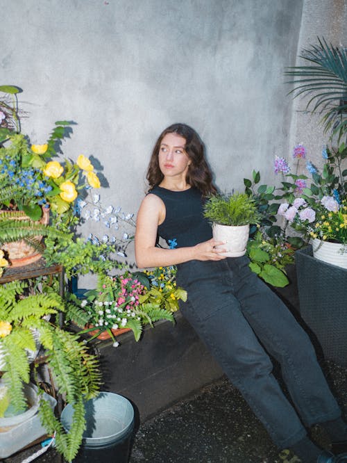Woman in Black Tank Top and Black Pants Holding a Potted Plant 
