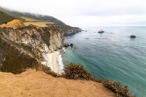 Free Scenic coastal cliffs overlooking a sandy beach and expansive ocean under cloudy skies. Stock Photo