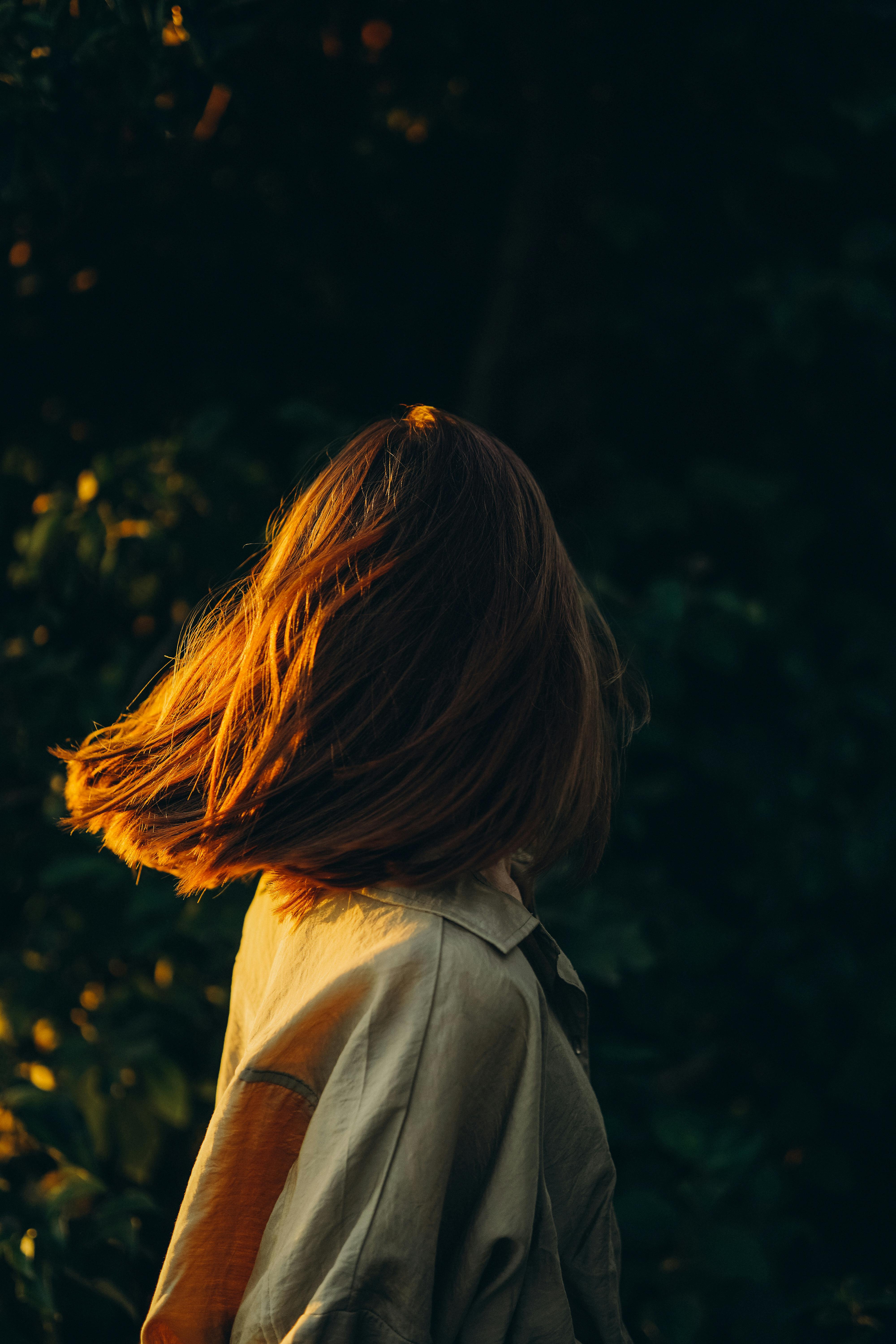 A woman flipping her hair outdoors in golden sunlight, creating a dynamic motion effect.
