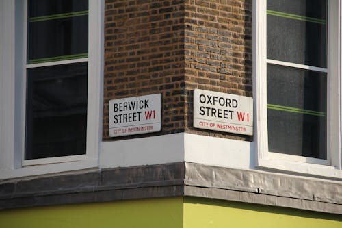 A Pair of Street Signs on Brown Brick Wall Beside Windows