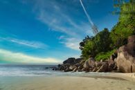 Serene beach with rocks and lush greenery in La Digue, Seychelles under a vibrant sky.