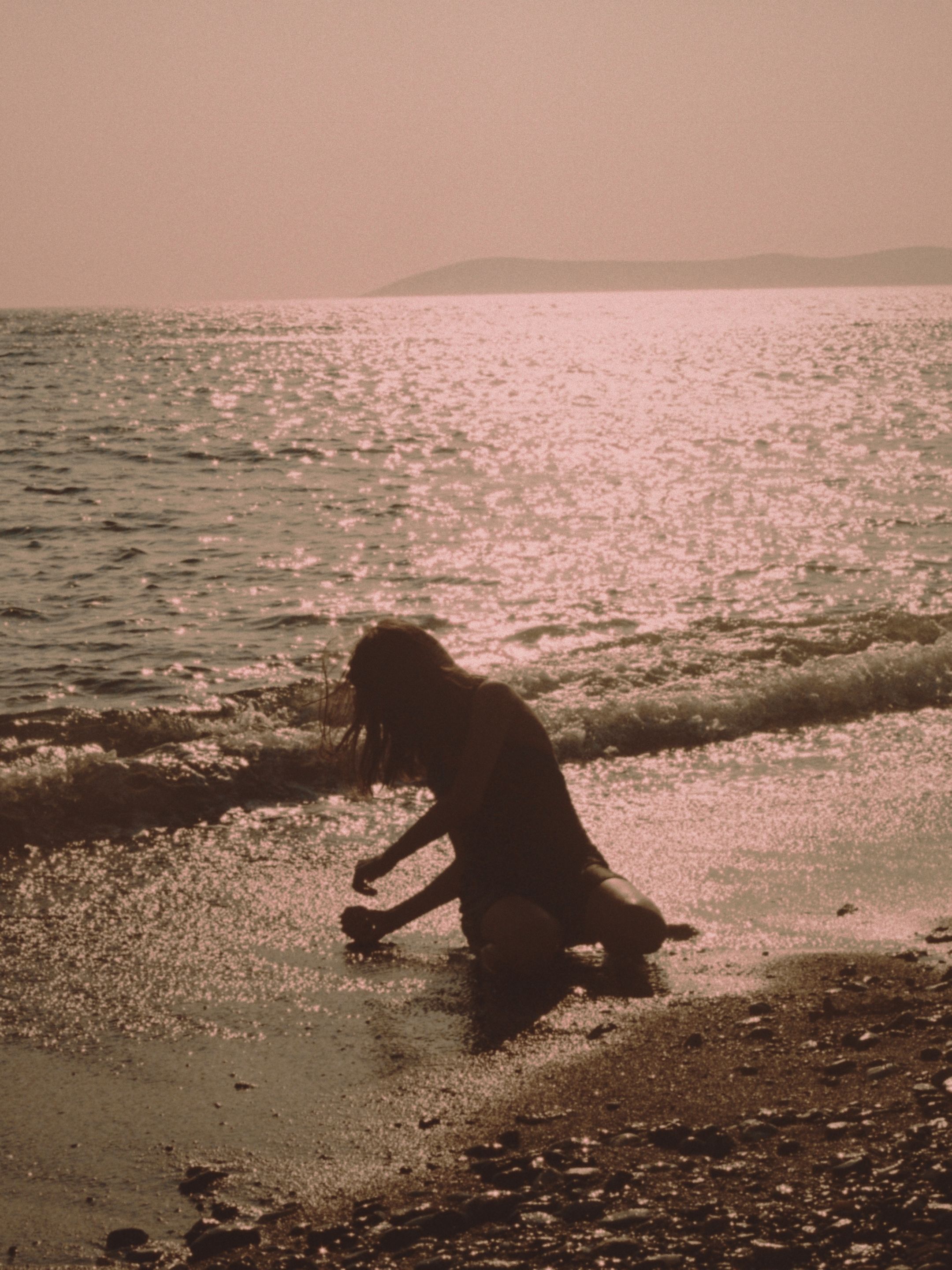 Silhouette of a woman sitting by the beach at sunset, enjoying the serene seaside atmosphere.