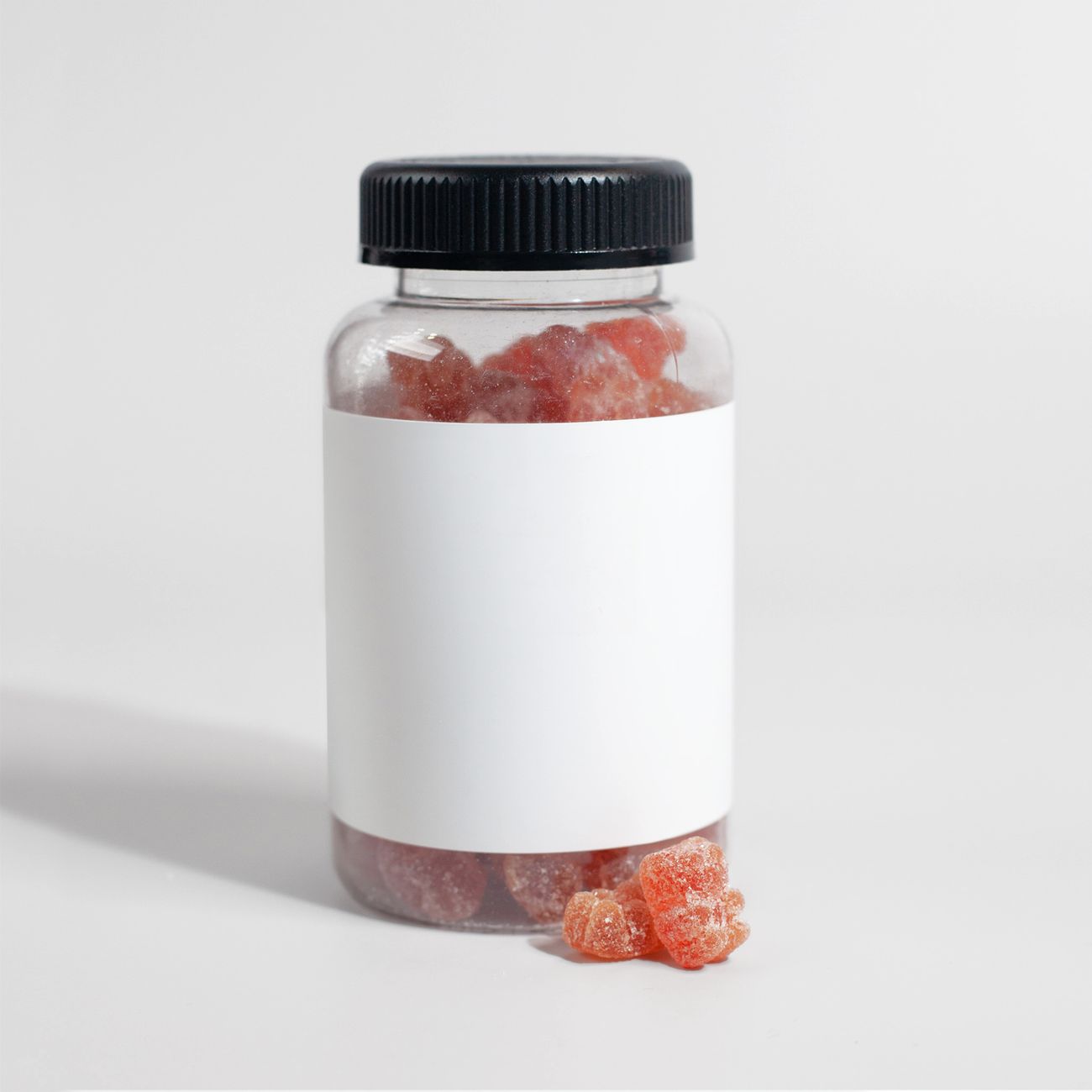 Close-up of a clear jar filled with gummy supplements, against a plain backdrop.