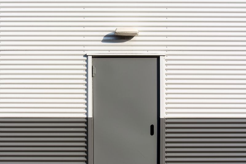 Minimalist image of a corrugated metal wall with a centered door, showcasing industrial architecture.