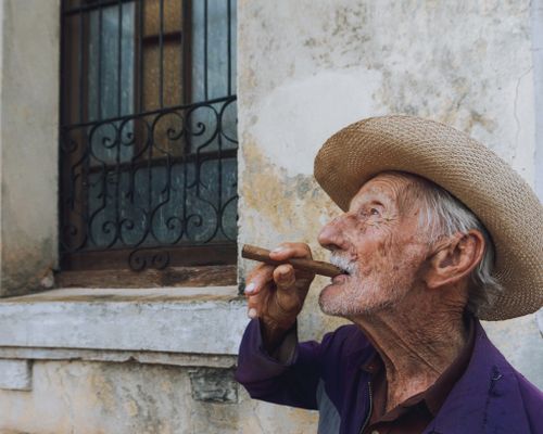 Free Senior man in a straw hat smoking a cigar against a rustic wall Stock Photo