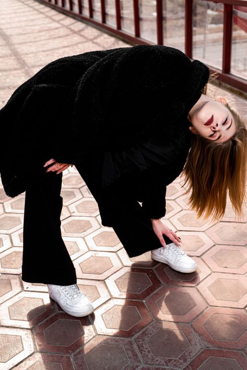 Free Stylish woman in black coat and white sneakers striking a unique pose. Stock Photo